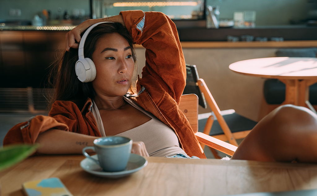 Mulher com o fone JBL Tune 520BT no ouvido enquanto toma café